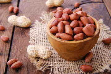 Raw peanuts in a scoop and a bowl on a wooden background.