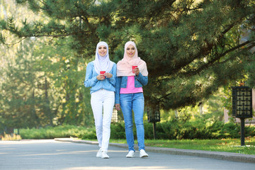 Wall Mural - Muslim women with cups of coffee walking in park