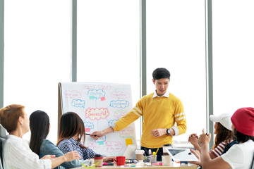 Young asian creative businessman standing and making presentation at modern office happy talking and brainstorming with team by pointing ideas on flipchart. Casual people business meeting concept.