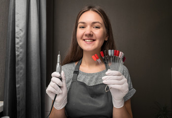 happy  young woman profession manicurist with  nail machine  and nail color palette on gray background