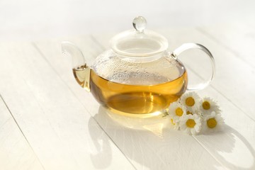 Chamomile tea in a  glass teapots and white daisy flowers on a white wooden board background.Organic teas for health