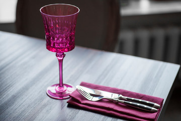 rose glass wine glass on a dark wooden table with a marsala-colored napkin and a fork and knife lying on it