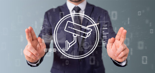 Poster - Businessman holding Security camera system icon and statistics data - 3d rendering
