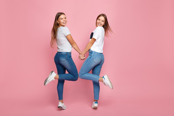 Happy two young twin sisters wit beautiful smile dance over pink background.