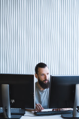 man working in office using two monitors. bearded hipster it specialist.