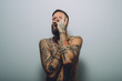 © Connect Images - Portrait of young man with beard, covered in tattoos, hand on face, screaming