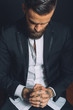 © Connect Images - Young man wearing suit, sitting with hands clasped, tattoos on hands, pensive expression