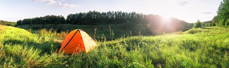 Wall Mural - orange tourist tent in the green grass under the setting sun