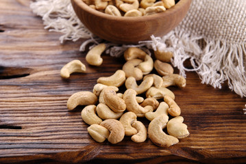 Wall Mural - Fried cashews in a bowl and scoop on a brown wooden table.