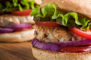 Close up of two homemade turkey burgers with salad, tomatoes, pickles and red onion