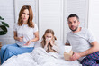 © LIGHTFIELD STUDIOS - parents taking care of sick daughter in bedroom, giving her pills and glass of water, looking at camera