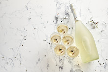 Champagne Glasses And Bottle Placed On White Marble Background. Party And Holiday Celebration Concept With Confetti And Serpentines. With Copy Space.