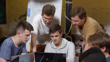 Group of young men discussing coding task together during programming workshop, one of them using laptop computer and showing something to the others