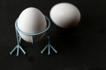 Two cooked organic eggs for breakfast one on a stand the other lies on a table on a black background