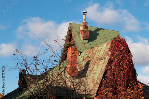 Fotografie, Obraz Goblin house with chimneys and bright red leaves of wild grape on an autumn sunn