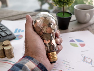 Wall Mural - hand of businessman hold light bulb with coin. concept of cost reduction and reduce energy