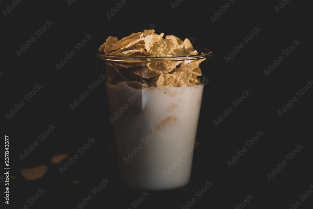 Corn flakes with milk in glass cup isolated on black