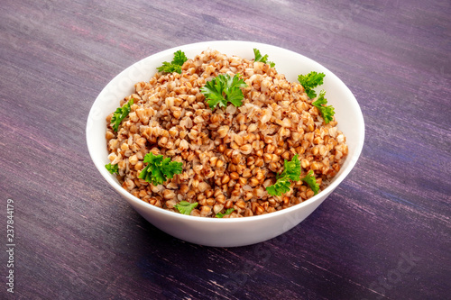 Fotografie, Obraz Cooked buckwheat in a bowl, garnished with fresh parsley, on a purple background