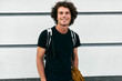 © iuricazac - Outdoor shot of handsome  smiling young man student with backpack standing at building background on the street. Businessman freelancer male wearing casual black t-shirt. People, education, business.
