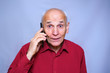 © Bonsales - senior man in a red shirt with a smartphone near the ear, surprised frightened look, talking on the phone