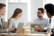 © fizkes - Millennial diverse employees talk brainstorming or collaborating at office meeting, workers sit at shared table with laptops cooperating at casual briefing, colleagues analyze statistics or paperwork