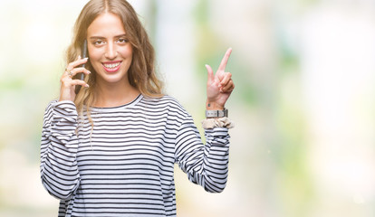 Wall Mural - Beautiful young blonde woman talking on smarpthone over isolated background surprised with an idea or question pointing finger with happy face, number one