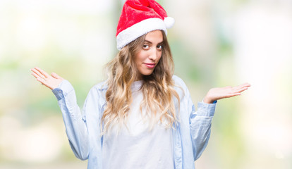 Poster - Beautiful young blonde woman wearing christmas hat over isolated background clueless and confused expression with arms and hands raised. Doubt concept.