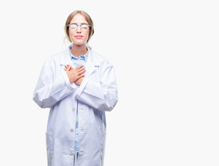 Poster - Beautiful young blonde doctor woman wearing white coat over isolated background smiling with hands on chest with closed eyes and grateful gesture on face. Health concept.