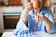 © Marina April - Graceful old hands. Senior woman is drinking hot beverage from mug in cozy home kitchen. Retired person is sitting and holding cup of coffee and spectacles. Grandmother with wedding ring has tea break