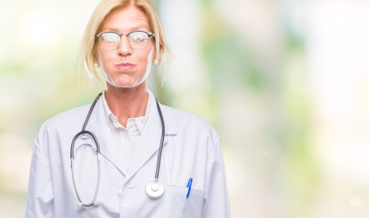 Sticker - Middle age blonde doctor woman over isolated background puffing cheeks with funny face. Mouth inflated with air, crazy expression.