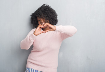 Poster - Young african american plus size woman over grey grunge wall wearing winter sweater smiling in love showing heart symbol and shape with hands. Romantic concept.