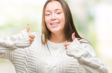 Young beautiful caucasian woman wearing winter sweater over isolated background success sign doing positive gesture with hand, thumbs up smiling and happy. Looking at the camera