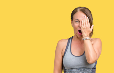 Beautiful middle age woman wearing sport clothes over isolated background covering one eye with hand with confident smile on face and surprise emotion.