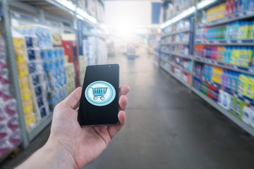 Hand holding mobile phone on Supermarket blur background. Shopping basket on a mobile phone screen. 