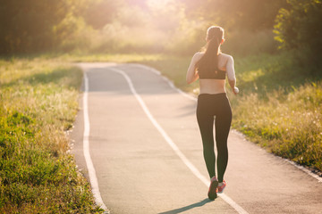 beautiful young sporty woman running on asphalt road in the Park in the morning