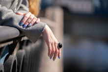 Close-up Of Hand In Grey Wool Coat With Blue Manicure With Huge Silver Ring With Round Black Stone On Fence Background
