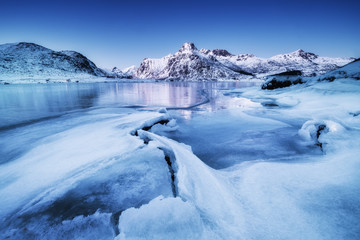 Wall Mural - Mountain ridge and ice on the frozen lake surface. Natural landscape on the Lofoten islands, Norway. Water and mountains during sunset.