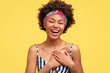 © WHstudio Leushin N - Positive dark skinned young woman with pleased expression, feels satisfied to hear compliment or confession in love, keeps both hands on chest, poses over yellow background, wears casual clothes