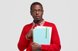 © wayhome.studio  - Stupefied dark skinned erudite being shocked to be asked unexpected question, holds textbooks and papers with pen, dressed in fashionable red jumper, isolated over white studio wall. Surprisement