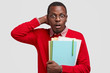 © WHstudio Leushin N - Waist up shot of emotive black young man scrathces head in bewilderment, has dark skin, realizes deadline for exam preparation, wears optical glasses, models over white wall. Education concept