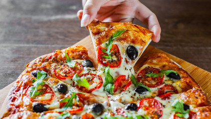 woman Hand takes a slice of Pizza Margherita or Margarita with Mozzarella cheese, tomato, olive. Italian pizza on wooden table background