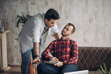 Wall Mural - European homosexual male couple enjoying leisure time together, sitting by table and watching online movie on laptop computer in the living room with monochrome interior