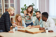 © alfa27 - Multiethnic young people sitting at table reading big book while sitting at the table in library. Students are preparing to the exams
