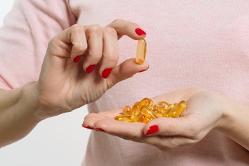 Wall Mural - Woman holding capsule with vitamin E, fish oil, Omega 3. White background, isolated, focus on the capsule