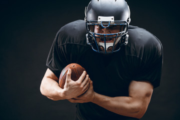 Wall Mural - American football sportsman player in black outfit and helmet runing, isolated on black background