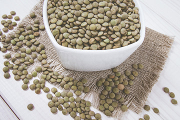 Green lentils in a bowl on a wooden background.