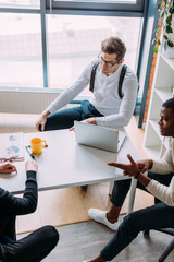 Canvas Print - High angle view of caucasian and african american coworkers discussing the project at table in office