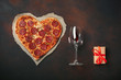 Heart shaped pizza with mozzarella, sausagered, wineglass, gift box on rusty background