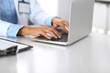© rogerphoto - Unknown doctor woman typing on laptop computer while sitting at the desk in hospital office. close-up of hands. Physician at work. Medicine and health care concept