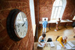 © pressmaster - Clock on red brick wall of modern office and several colleagues working individually by tables